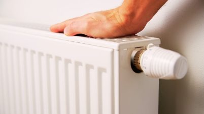 Devez-vous éteindre ou baisser votre chauffage pendant votre absence ? une main posée sur un radiateur